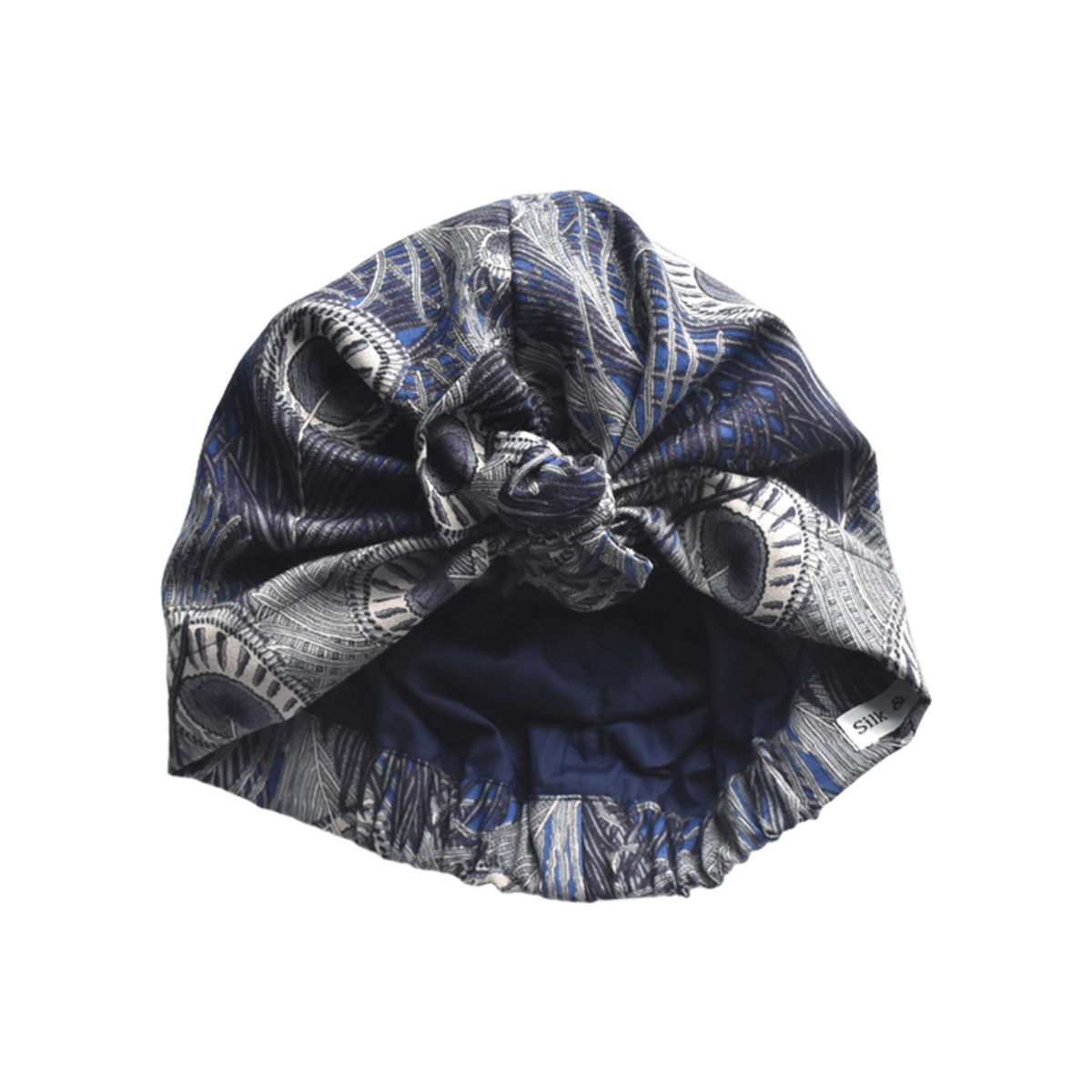 A knotted fabric headwrap or turban-style hair accessory in Vintage Liberty Hera Feather in Lapis blue   - Varuna Wool / peacock feather blue, gray, and white pattern, shown on a plain white background.