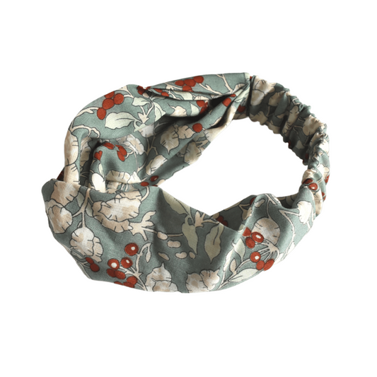 A fabric headband with a twisted knot design, featuring a muted sage green background with a floral pattern of white flowers and small red berries, shown on a plain white background.